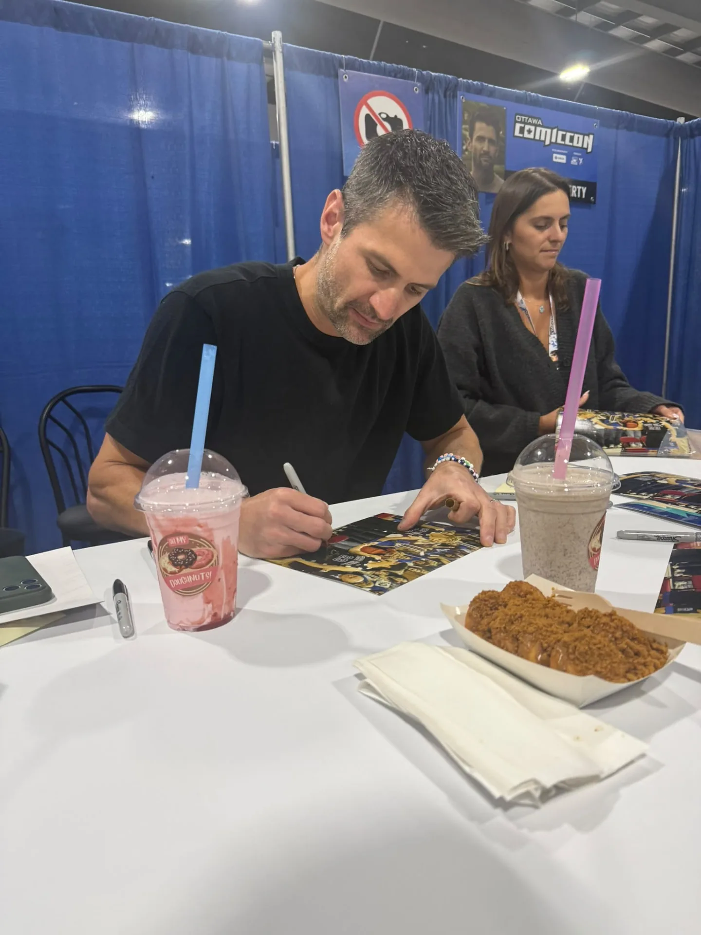 Comiccon guest signing beside Oh My Doughnuts and branded milkshakes